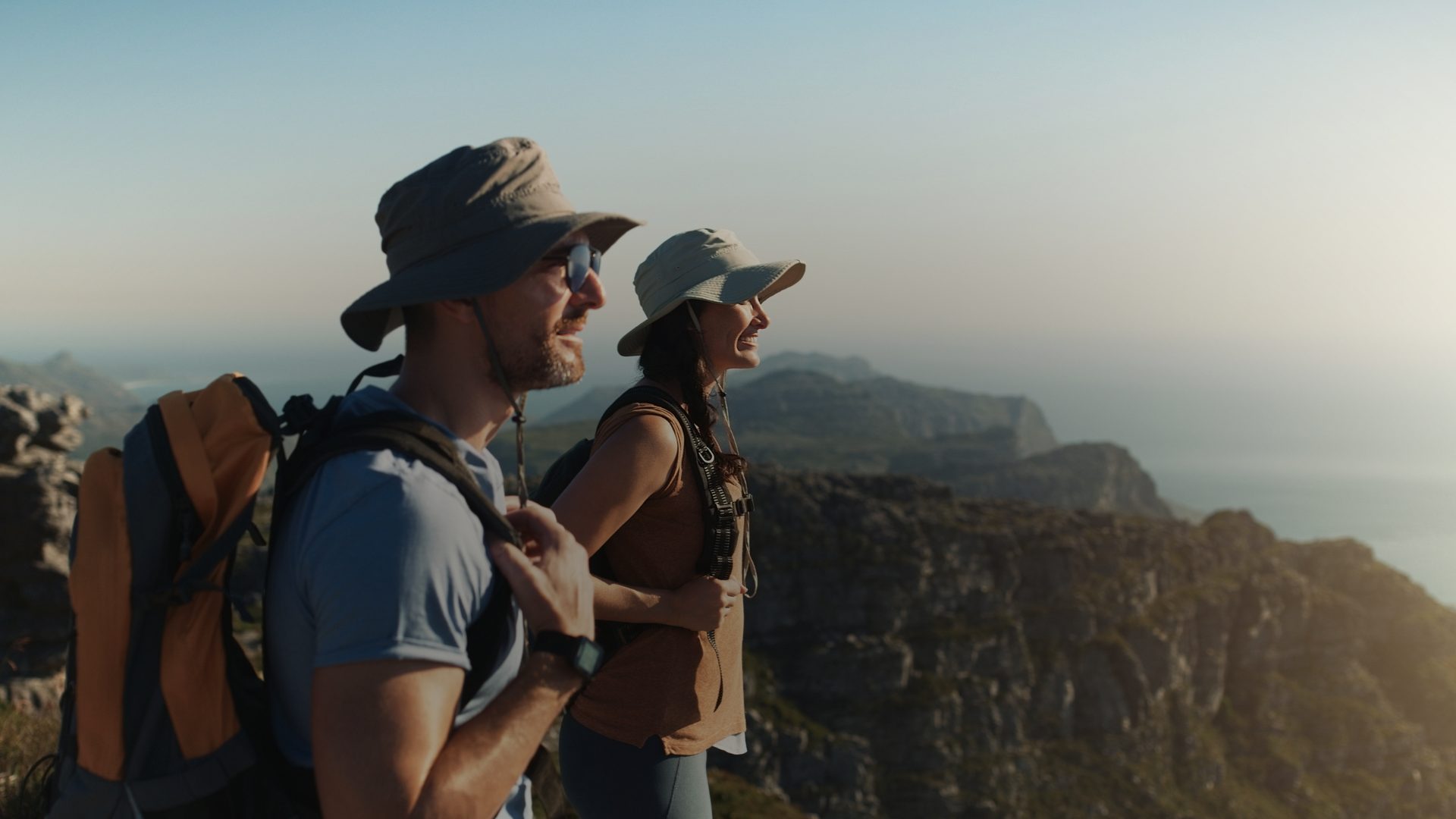 Casal de viajantes caminhando por uma trilha nas montanhas ao pôr do sol